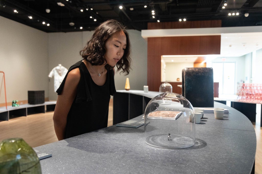 Young woman in a gallery bends to look at a ring made of distilled smog under a case