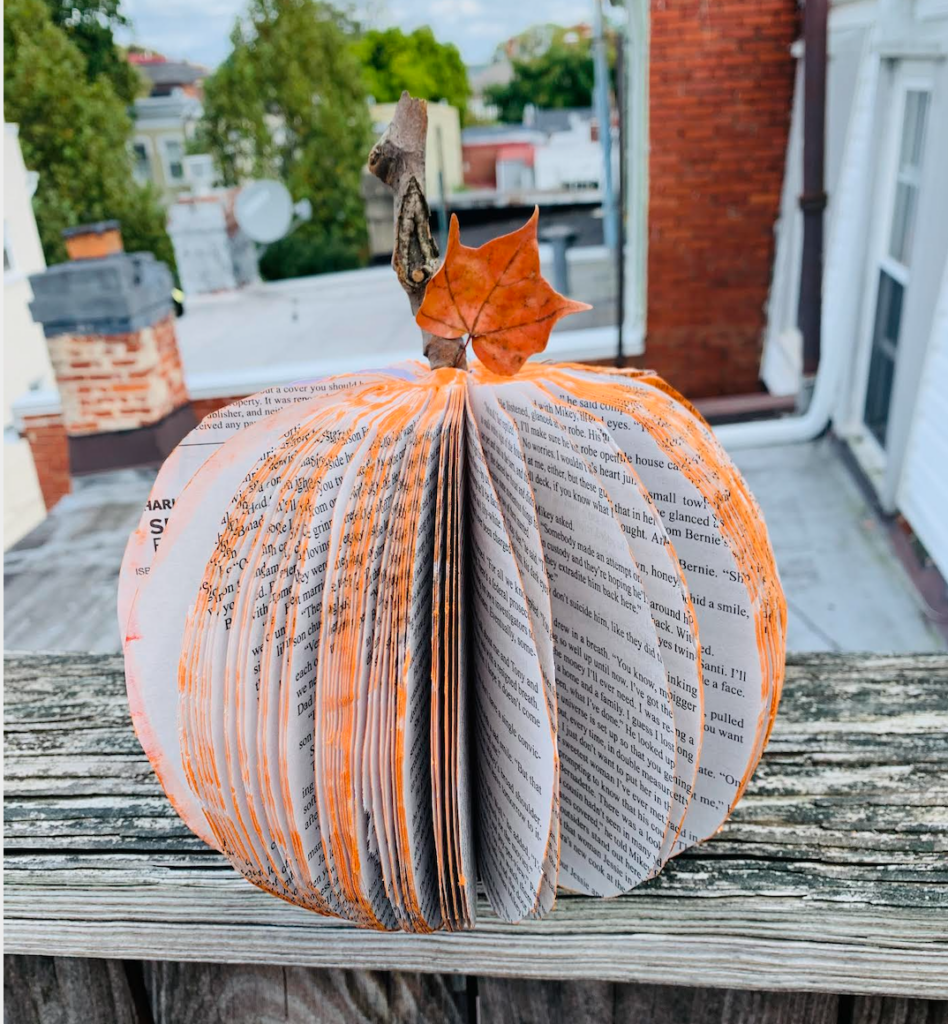 A book cut into the shape of a pumpkin with an orange leaf attached to the stem.