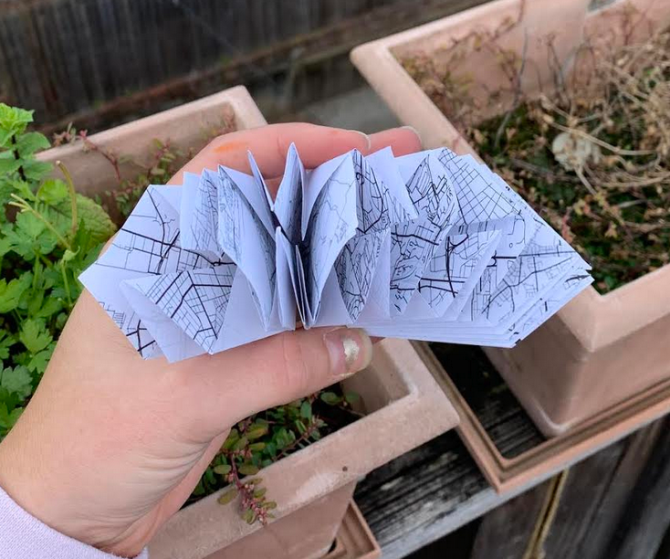 A hand holds open a map folded into an intricate origami book. 