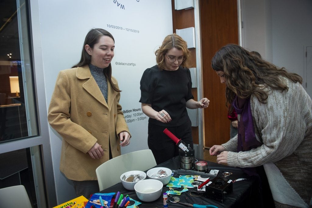 Three students outside a gallery working at a table covered in art supplies