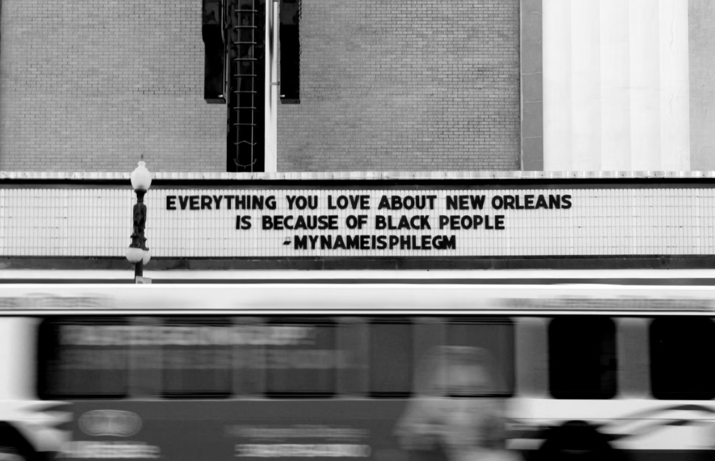 A black and white picture of a theatre marquee that reads Everything you love about new orleans is because of black people - my name is phlem