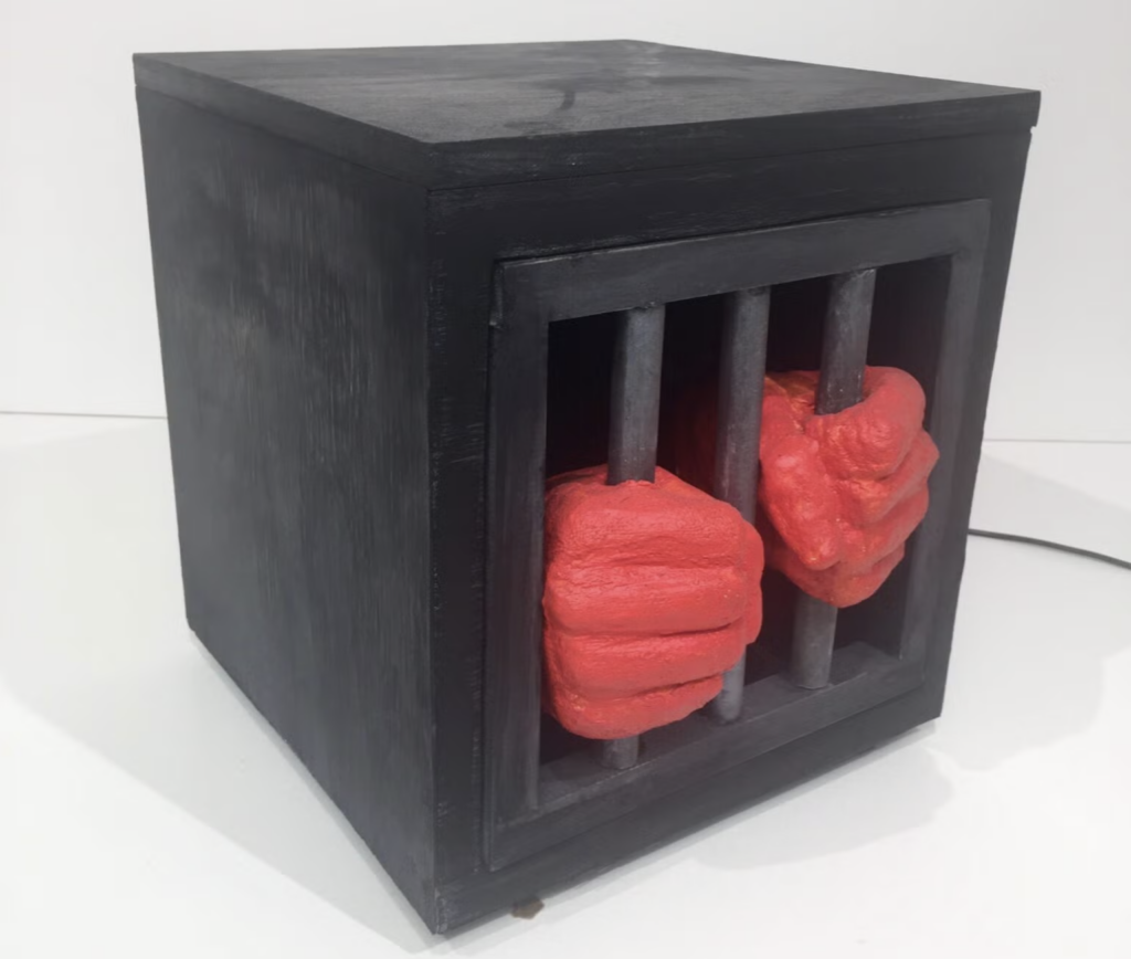 Black box with bars and red hands grabbing the bars from within. 