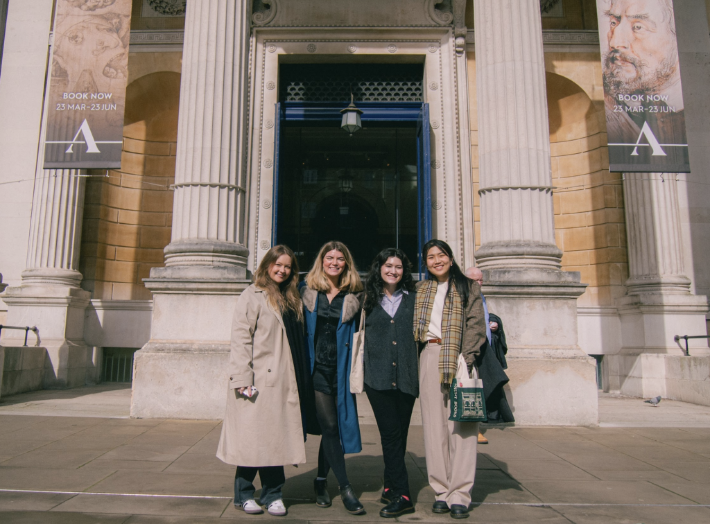 Four women stand in front of a London museum entrance on a sunny day.